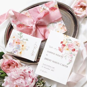 May include: A wedding invitation with a watercolor floral design in shades of pink, yellow, and green. The invitation reads "Together with you, Daphne Wilson & Jeremy Mason Carter, At the Floral Cafe, 21 December, 2023".