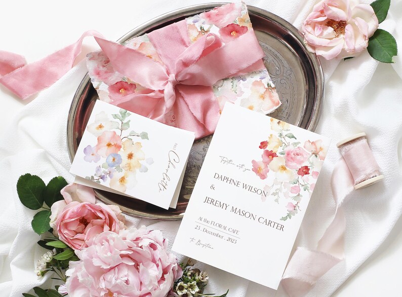 May include: A wedding invitation with a watercolor floral design in shades of pink, yellow, and green. The invitation reads "Together with you, Daphne Wilson & Jeremy Mason Carter, At the Floral Cafe, 21 December, 2023".