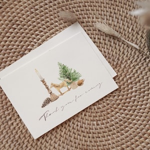 May include: A white folded greeting card featuring a watercolor illustration of a lit candle, a pinecone, a small horse figurine, a green pine tree, and a round ornament. The text "Thank you for coming" is printed in a black cursive script below.