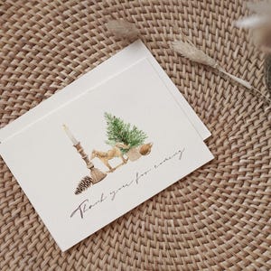 May include: A white folded greeting card featuring a watercolor illustration of a lit candle, a pinecone, a small horse figurine, a green pine tree, and a round ornament. The text "Thank you for coming" is printed in a black cursive script below.