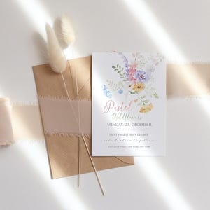 May include: A floral invitation card with the text "Pastel Wildflowers" and event details. The card features watercolor flowers in pastel colors. A brown envelope with a pink ribbon and dried flowers are also in the image.