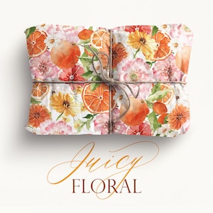 May include: A gift box wrapped in white paper with a floral and citrus pattern. The paper features watercolor illustrations of oranges, lemons, and pink and yellow flowers. The box is tied with twine.