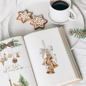 May include: An open book featuring watercolor illustrations of gold Christmas ornaments, bells, and pine branches, with the text "GOLD christmas" printed on the left page, accompanied by a white mug of coffee and two star-shaped cookies.