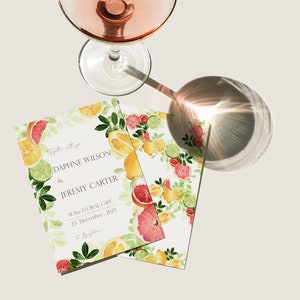 May include: A wedding invitation with a citrus fruit theme. The invitation is printed on white cardstock and features a watercolor illustration of lemons, limes, grapefruits, and leaves. The text on the invitation reads "Together with you, Daphne Wilson & Jeremy Carter, At the Floral Cafe, 23. December. 2023, to Beugatine."