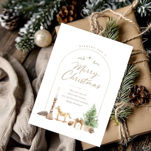 May include: A white rectangular greeting card featuring a gold arched frame with the text "Wishing you a Merry Christmas" and "May your days be filled with warmth, joy, and cherished moments. Happy Holidays!" alongside watercolor illustrations of a candle, a rocking horse, a gift, and a pine tree.