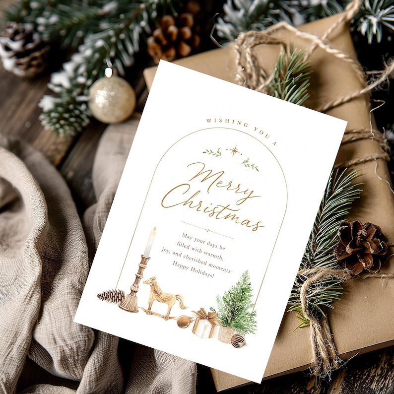 May include: A white rectangular greeting card featuring a gold arched frame with the text "Wishing you a Merry Christmas" and "May your days be filled with warmth, joy, and cherished moments. Happy Holidays!" alongside watercolor illustrations of a candle, a rocking horse, a gift, and a pine tree.