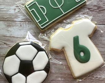 Könnte beinhalten: Drei verzierte Zuckerkekse: ein Fußball, ein Fußballfeld und ein weißes Fußballtrikot mit der Nummer 6 in Grün.