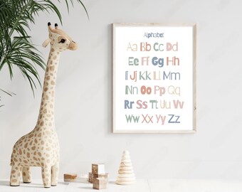 May include: A framed alphabet chart with pastel colored letters. The letters are in a playful font and are arranged in alphabetical order. The chart is hanging on a white wall next to a stuffed giraffe toy.