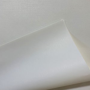 May include: A close-up of a white textured surface with a white sheet of paper folded over the top edge. The paper is smooth and has a slight sheen.