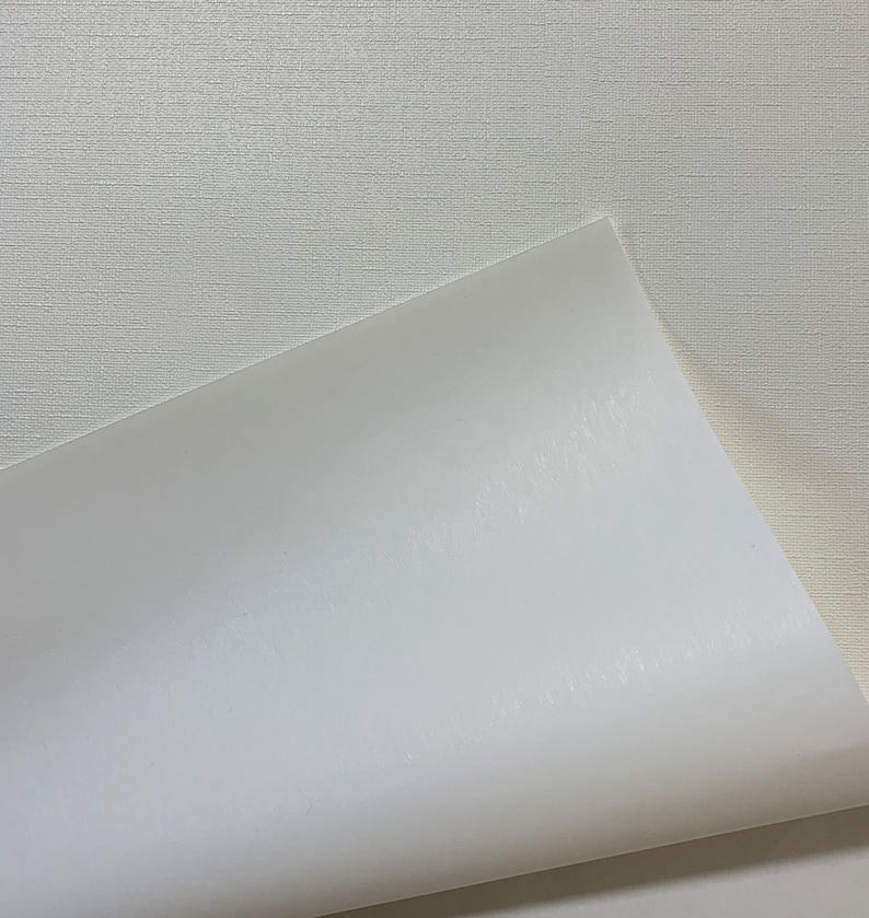 May include: A close-up of a white textured surface with a white sheet of paper folded over the top edge. The paper is smooth and has a slight sheen.