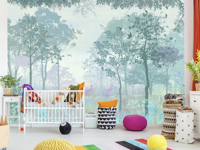 K&ouml;nnte beinhalten: Ein Kinderzimmer mit einem Wald-Themen-Wandbild in Blau- und Gr&uuml;nt&ouml;nen. Im Vordergrund befindet sich ein wei&szlig;es Kinderbett, das mit bunten Kissen und Pompons dekoriert ist. Weitere Dekorationen sind ein schwarz-wei&szlig; gemusterter Korb, ein rosa Pouf und ein schwarzes 8-Ball-Kissen.