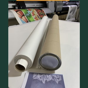May include: Two rolled canvases are being packaged in cardboard tubes. One canvas is white and the other is printed with a colorful design. The tubes are on a white surface.