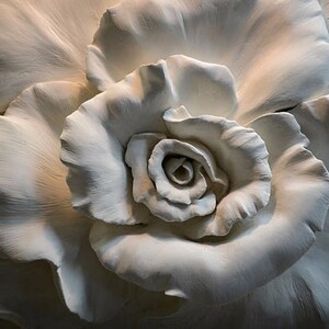 Op de afbeelding: Een witte gipsen rozen sculptuur met gedetailleerde bloemblaadjes en een centrale knop. De sculptuur is een driedimensionale weergave van een roos.