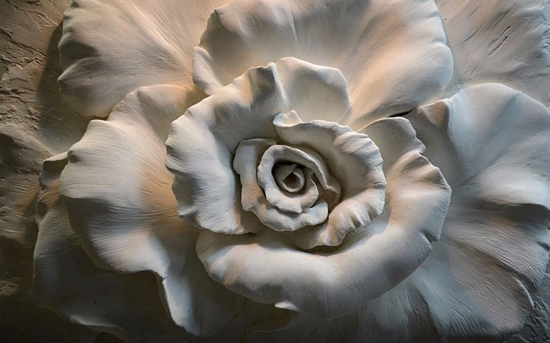 Op de afbeelding: Een witte gipsen rozen sculptuur met gedetailleerde bloemblaadjes en een centrale knop. De sculptuur is een driedimensionale weergave van een roos.