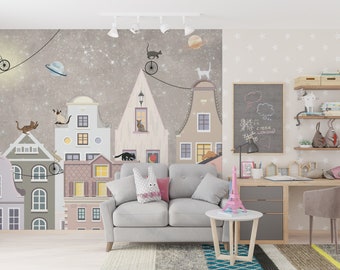 May include: A whimsical mural featuring a cityscape with cats on rooftops, planets, and a starry sky. The room includes a gray sofa, a desk, and decorative shelves with books and toys. A pink Eiffel Tower model sits on a small table.