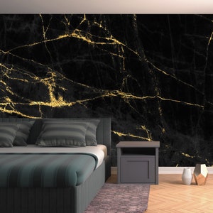 May include: A bedroom with a black and gold marble patterned wallpaper, a bed with a dark green striped duvet, two pillows, and a nightstand with a lamp.
