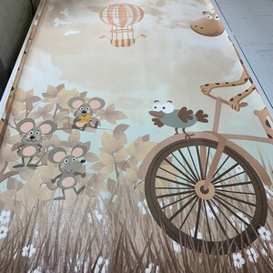May include: A beige and brown wallpaper with a whimsical design featuring a hot air balloon, a plane, a giraffe riding a bicycle, a bird, and three mice. The wallpaper has a textured, fabric-like appearance.