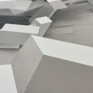 May include: A close-up of a white geometric shape with a textured surface. The shape is made up of multiple smaller shapes that are arranged in a random pattern.