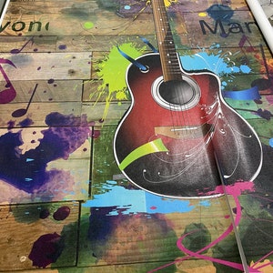 Op de afbeelding: Een rode akoestische gitaar met zwarte en witte details is geschilderd op een houten achtergrond met kleurrijke verfspatten. De woorden "Rock" en "Mar" zijn zichtbaar op de achtergrond.