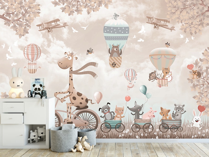 May include: A whimsical nursery wall mural featuring a giraffe riding a bicycle, animals in hot air balloons, and a bunny rabbit. The mural is set against a light brown background with clouds and trees.