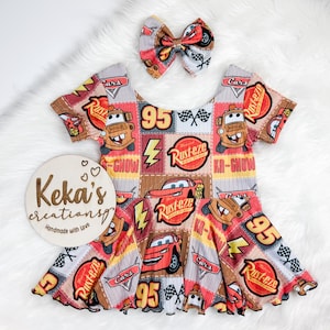 May include: A children's dress and matching bow featuring a Cars movie theme. The dress has a patchwork design with images of Lightning McQueen, Mater, and the Rust-eze logo. The dress is red, brown, and grey.