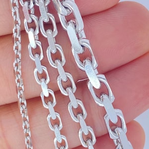 May include: A close-up of several silver-colored chain necklaces. The chains vary in style, with different link designs, including oval and rectangular shapes. The necklaces are held in a hand against a white background.