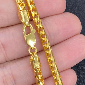 May include: A gold chain necklace with a lobster clasp. The chain is a Franco chain style, which is a flat, woven chain.