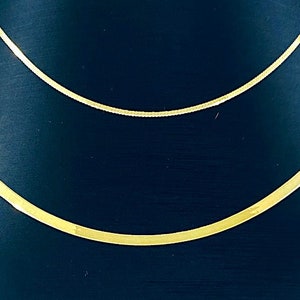 Puede incluir: Dos collares de cadena de oro en un expositor negro. Las cadenas est&aacute;n superpuestas, con la cadena m&aacute;s gruesa en la parte inferior.