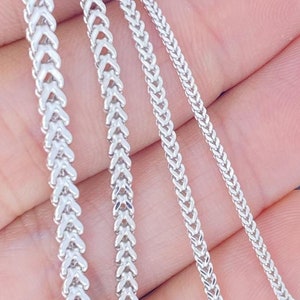 May include: Four silver chains of different lengths and widths, all with a herringbone pattern, are displayed on a hand.