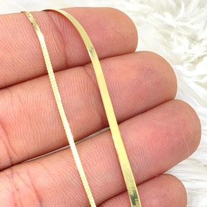 Puede incluir: Dos cadenas de oro, una con una superficie plana y lisa y la otra con una superficie texturizada, se sostienen en una mano.