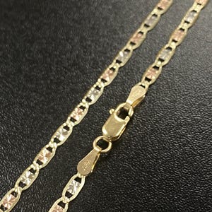 K&ouml;nnte beinhalten: Eine goldene Halskette mit dreifarbigem Design, mit gelben, rosafarbenen und wei&szlig;en Goldgliedern. Die Kette wird mit einem Verschluss vor dunklem Hintergrund gezeigt. Die Halskette ist ein Schmuckst&uuml;ck.