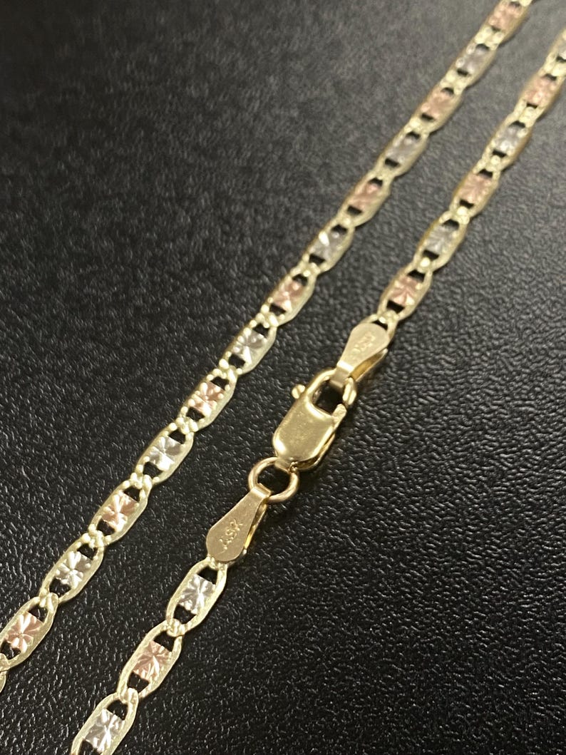 K&ouml;nnte beinhalten: Eine goldene Halskette mit dreifarbigem Design, mit gelben, rosafarbenen und wei&szlig;en Goldgliedern. Die Kette wird mit einem Verschluss vor dunklem Hintergrund gezeigt. Die Halskette ist ein Schmuckst&uuml;ck.