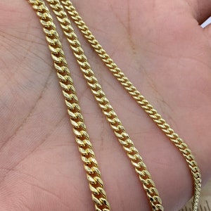 May include: Three gold chains of different lengths and widths. The chains are laid out on a hand, with the thickest chain on the bottom and the thinnest chain on the top.