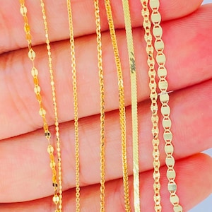 May include: Close-up of several delicate gold necklaces with various chain styles. The chains include oval links, thin strands, and a herringbone design. The jewelry is displayed against a light background.