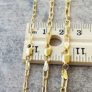 May include: Three gold chains of different lengths, laid out on a wooden ruler. The chains are all the same style, with a flat, oval-shaped link. The ruler is marked in inches and shows that the chains are 18 inches, 20 inches, and 22 inches long.