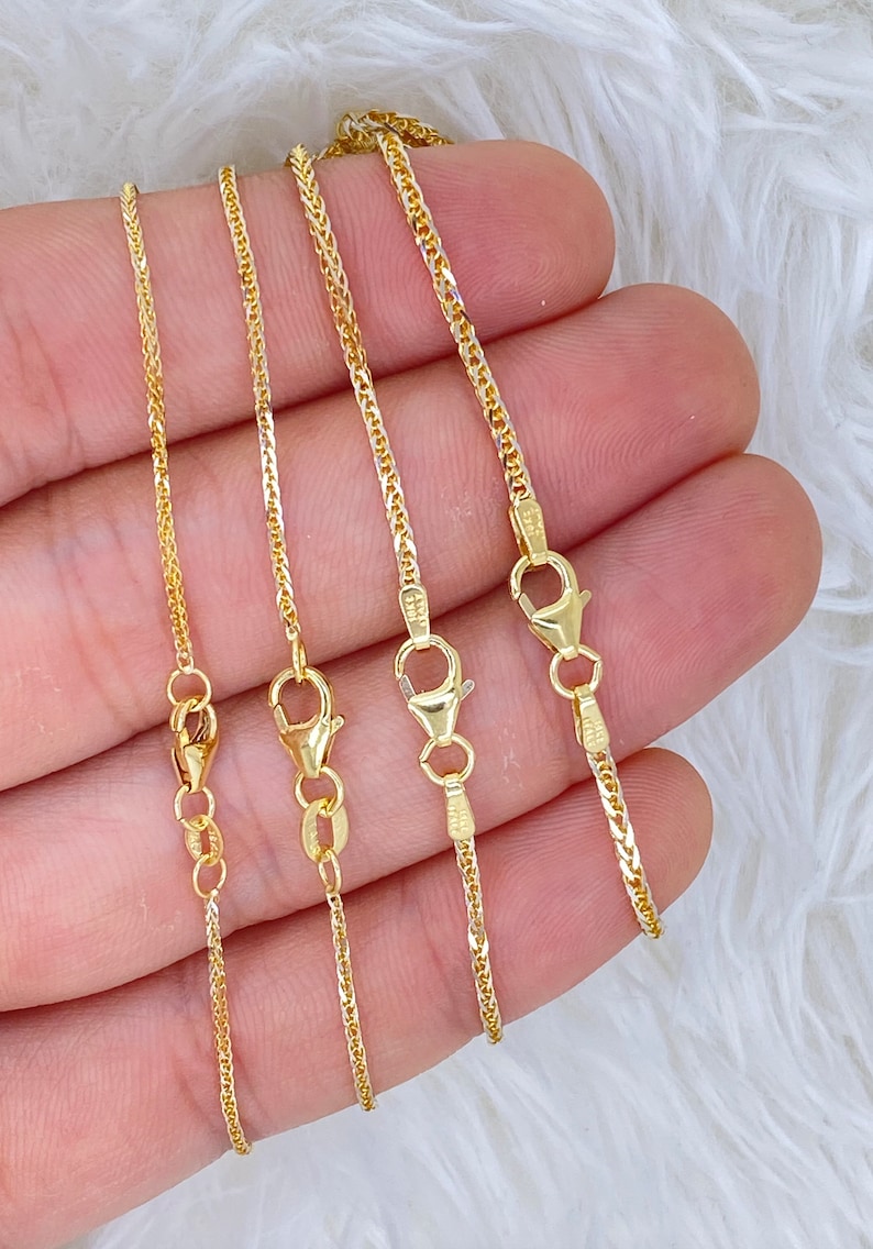May include: Four gold chains of different lengths, all with a box clasp. The chains are arranged in order of length, with the shortest chain on the left and the longest chain on the right.