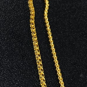 May include: Close-up of two gold-colored chain necklaces. The chains have a textured, woven design. The background is a dark, textured surface. The chains are likely jewelry.