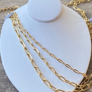 May include: Three gold chain necklaces of different lengths and widths, displayed on a white mannequin bust.