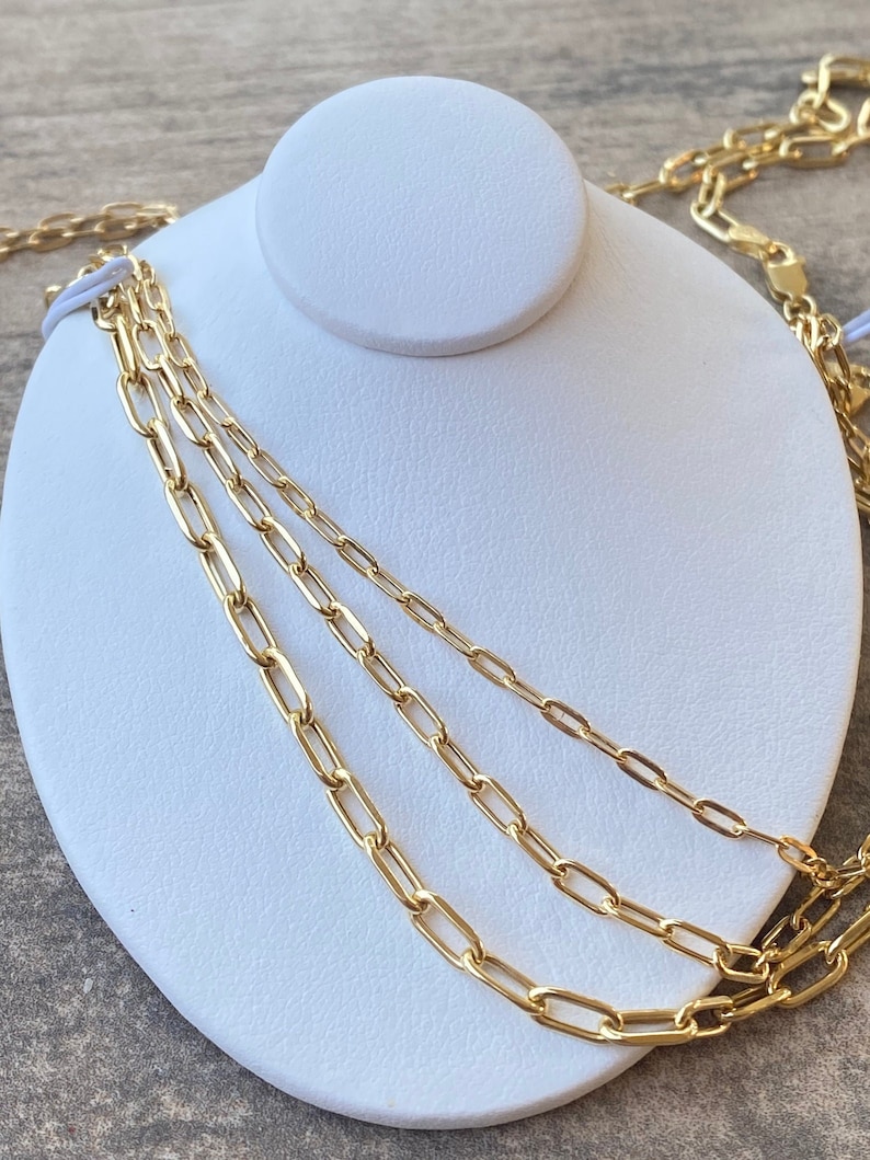 May include: Three gold chain necklaces of different lengths and widths, displayed on a white mannequin bust.