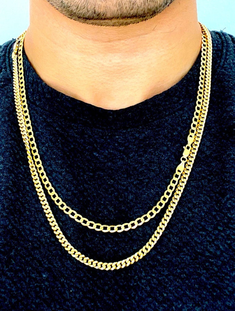 May include: Two gold chains, one thicker than the other, layered on a person's neck. The chains are both made of a classic curb link style.