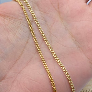 May include: Two gold chains of different thicknesses, one thicker than the other, are laid out on a person's hand. The chains are both made of a shiny gold metal.