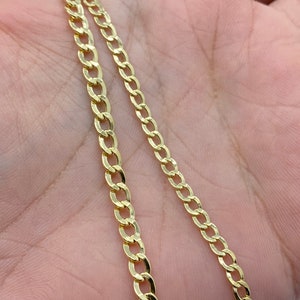 May include: A gold chain necklace with a curb link style. The chain is shown on a person's hand.
