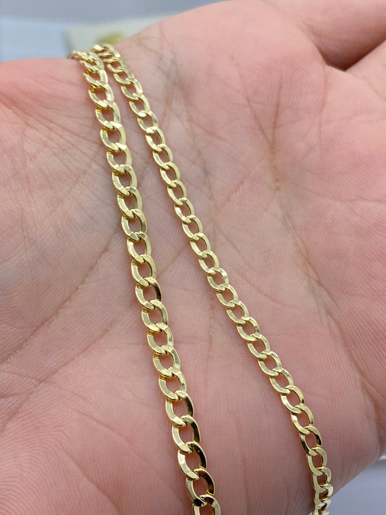 May include: A gold chain necklace with a curb link style. The chain is shown on a person's hand.