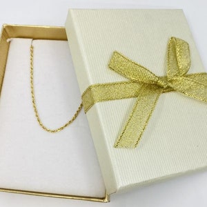Puede incluir: Un collar de cadena de oro en una caja de regalo blanca con una cinta dorada.