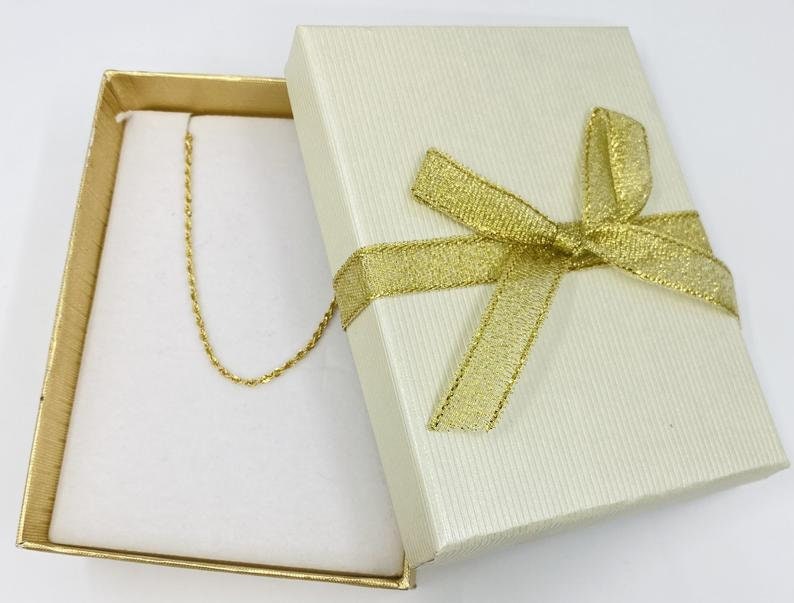 Puede incluir: Un collar de cadena de oro en una caja de regalo blanca con una cinta dorada.