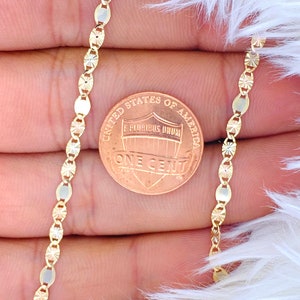 Puede incluir: Un collar de cadena de oro con un dise&ntilde;o de corte de diamante. La cadena se muestra junto a un centavo estadounidense para referencia de tama&ntilde;o.