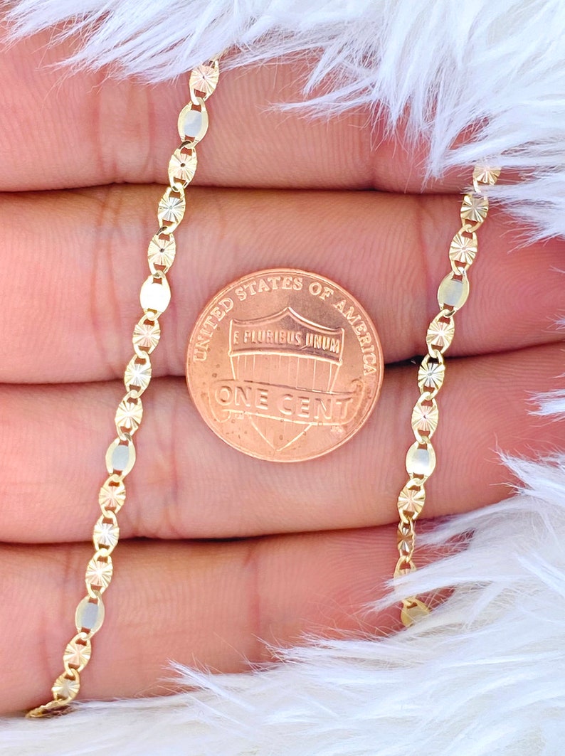 Puede incluir: Un collar de cadena de oro con un dise&ntilde;o de corte de diamante. La cadena se muestra junto a un centavo estadounidense para referencia de tama&ntilde;o.