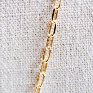 May include: A gold chain necklace with oval links. The chain is lying on a white fabric background.