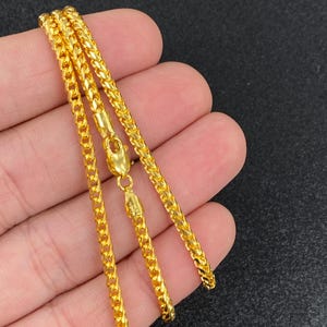 May include: A gold chain necklace with a Cuban link style. The chain is shown folded in half, with the clasp visible.