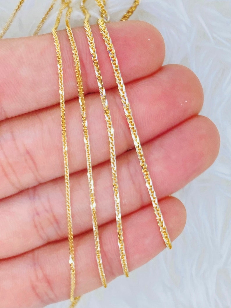 May include: Five gold chains of varying lengths and widths, displayed on a hand.